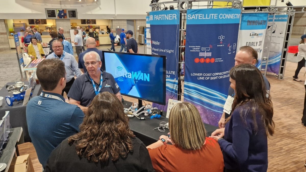 ACE 2025 attendees watching satellite-connected LoRaWAN water meter demonstration at Zenner USA, EchoStar Mobile and Semtech booth