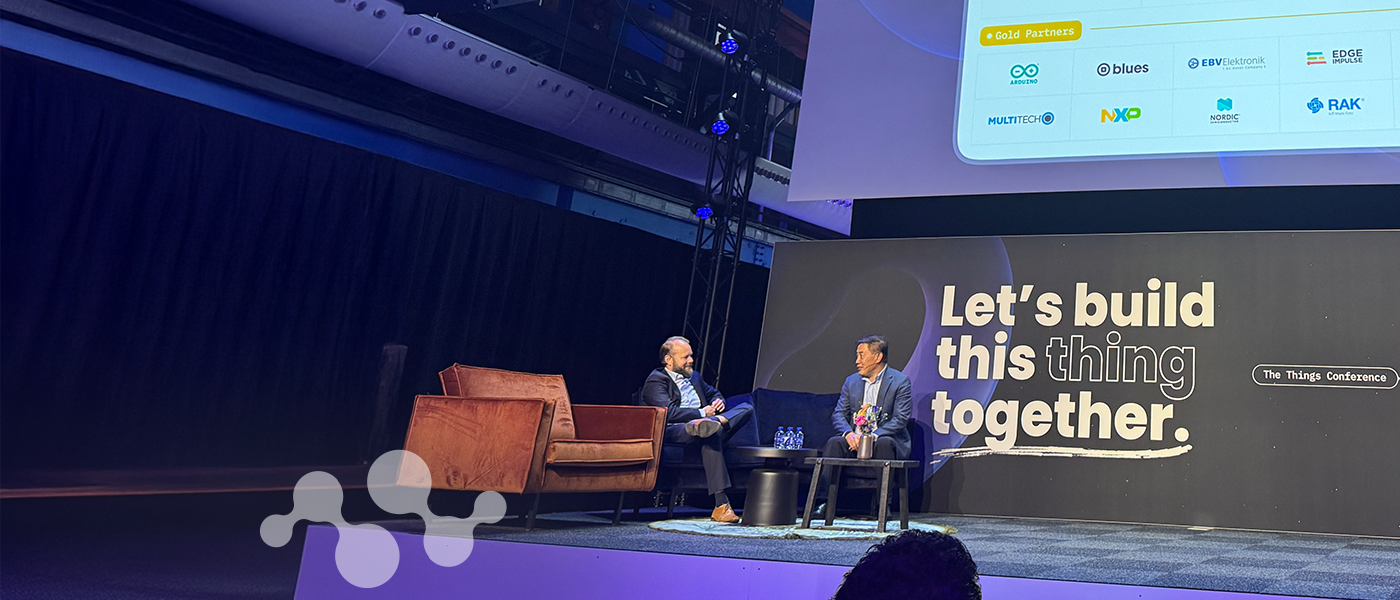 Panel discussion at The Things Conference 2025 with two speakers (Semtech's Dr. Hong Hou) on stage and "Let's build this thing together" messaging displayed on screen with IoT partner logos, audience seated in foreground