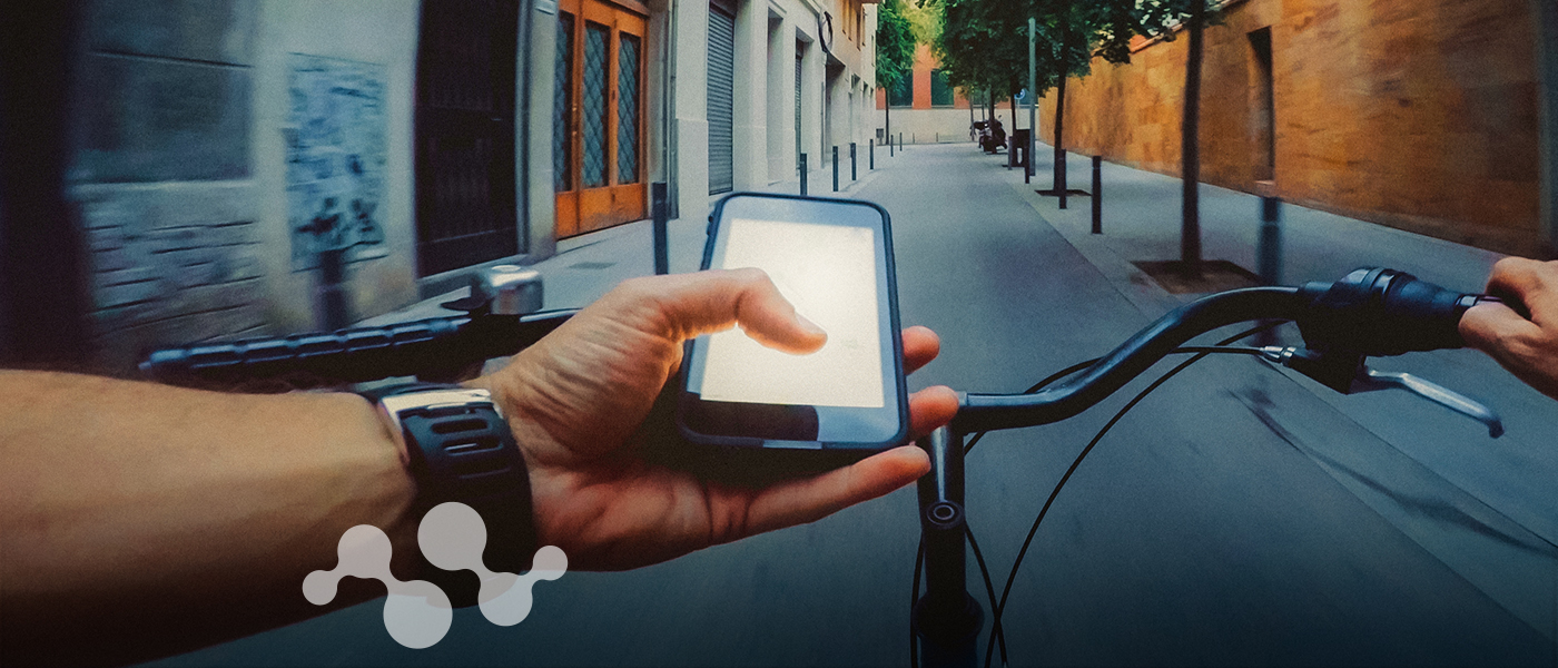 First-person view of rider using smartphone while cycling through urban street, showcasing connected e-bike technology and smart micromobility integration in city transportation.